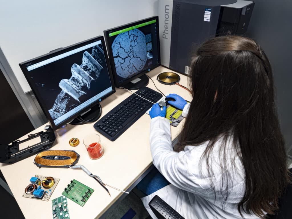 Technician performing microscopic analysis to identify unknown residues in an electrical component through materials characterization.