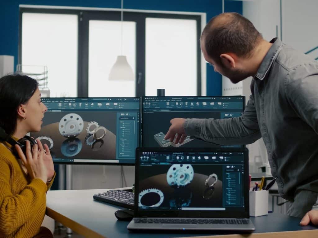 Escaneado 3D y digitalización de piezas Dos ingenieros revisando modelos CAD 3D de engranajes y componentes mecánicos en software industrial de diseño