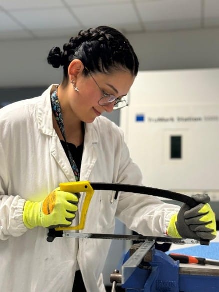 Researcher cutting metal samples in a laboratory to prepare specimens for corrosion testing and steel coating characterization.