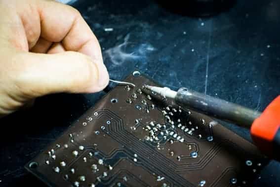 PCB failure analysis to improve the reliability of temperature sensors Technician inspecting and reworking solder joints on printed circuit board PCB during electronic failure analysis