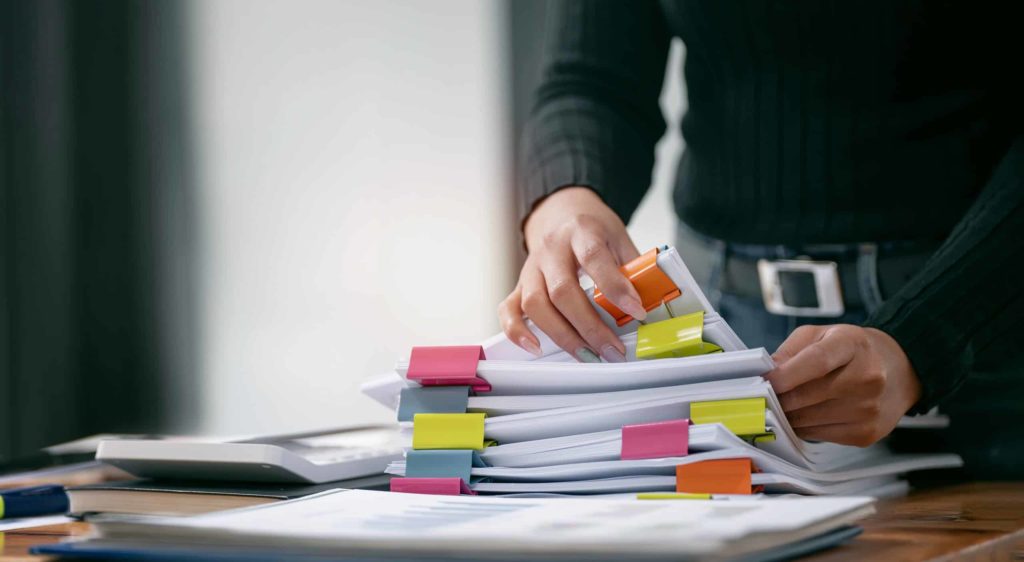 Manos revisando documentos técnicos señalizados con marcadores durante la preparación de un informe pericial