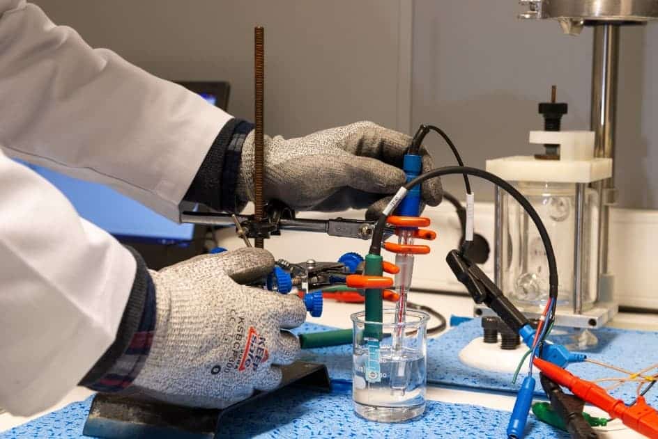 Technician wearing protective gloves connecting electrodes to a prototype reactor during laboratory testing