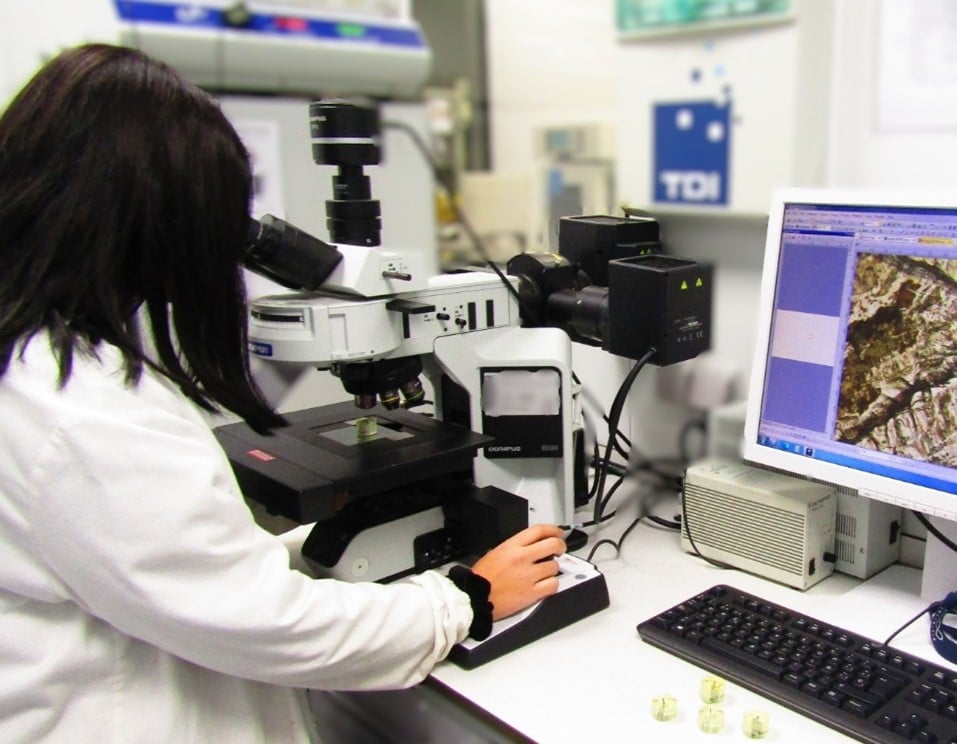 Ingeniera analizando una muestra metálica con microscopio para investigar la causa de fallo en un componente