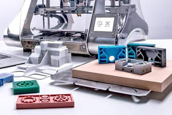 Impresora 3D de doble extrusor fabricando piezas de prototipo junto a otras piezas ya impresas