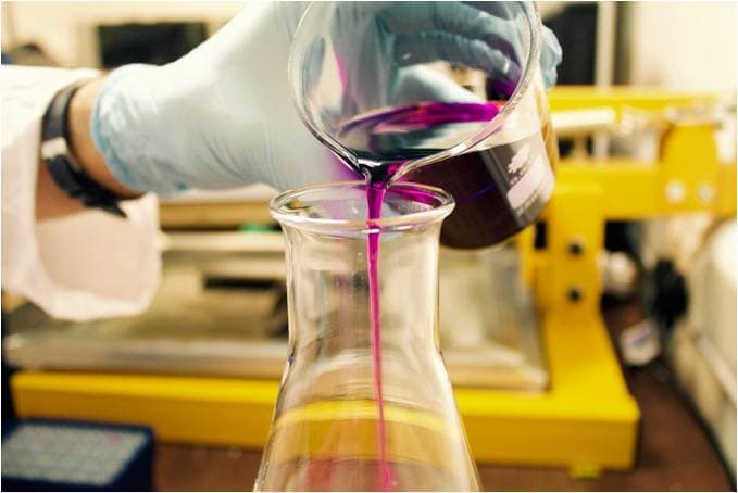 Desarrollo de producto mediante fabricación de moldes para elastómeros e impresión 3D Técnico vertiendo un líquido rosa en un matraz Erlenmeyer durante la preparación de materiales en laboratorio